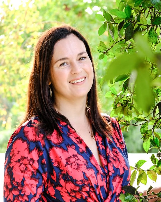 Elanza, smiling, standing in a leafy garden